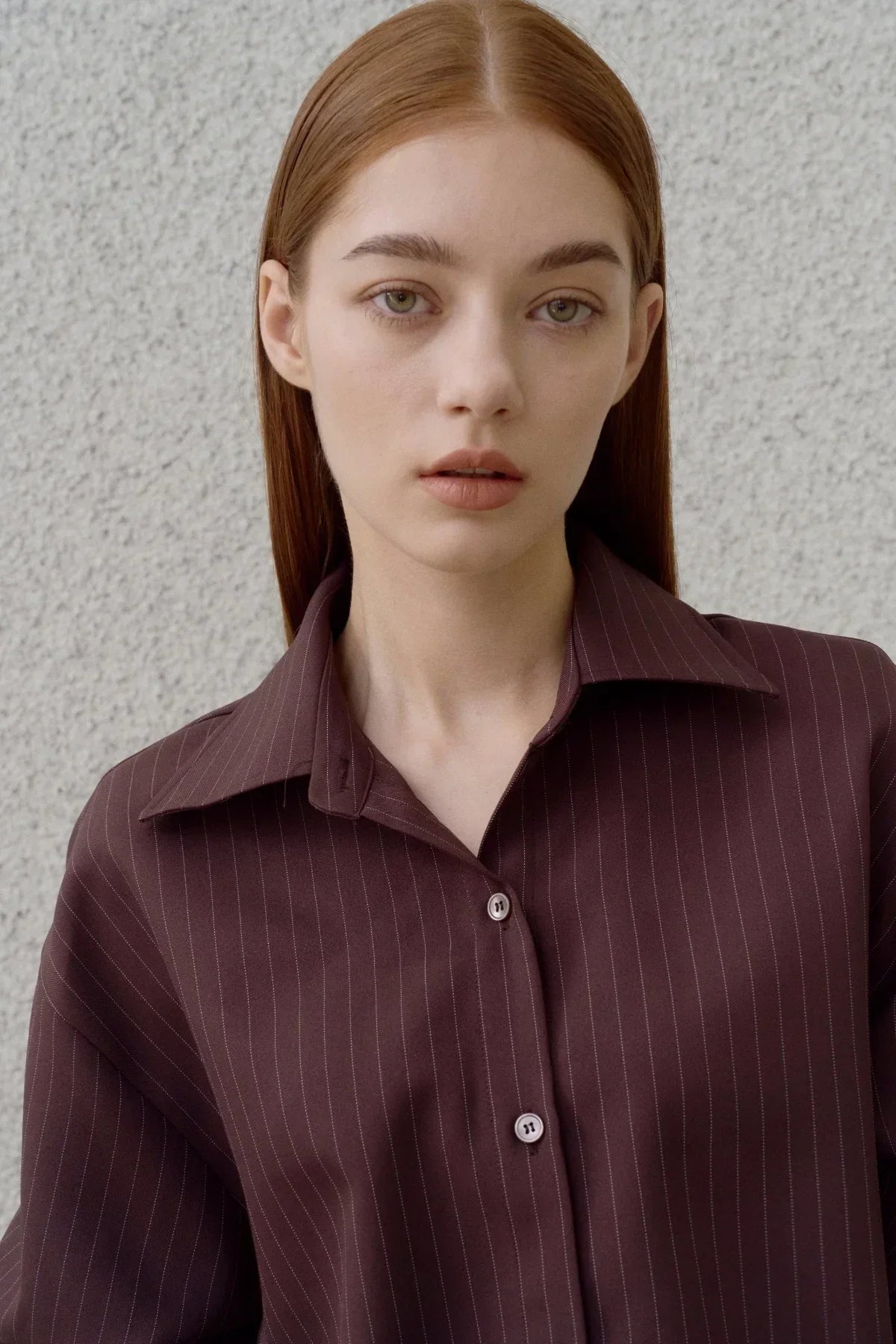 Close-up of woman wearing brown pinstripe shirt with buttons against light textured wall