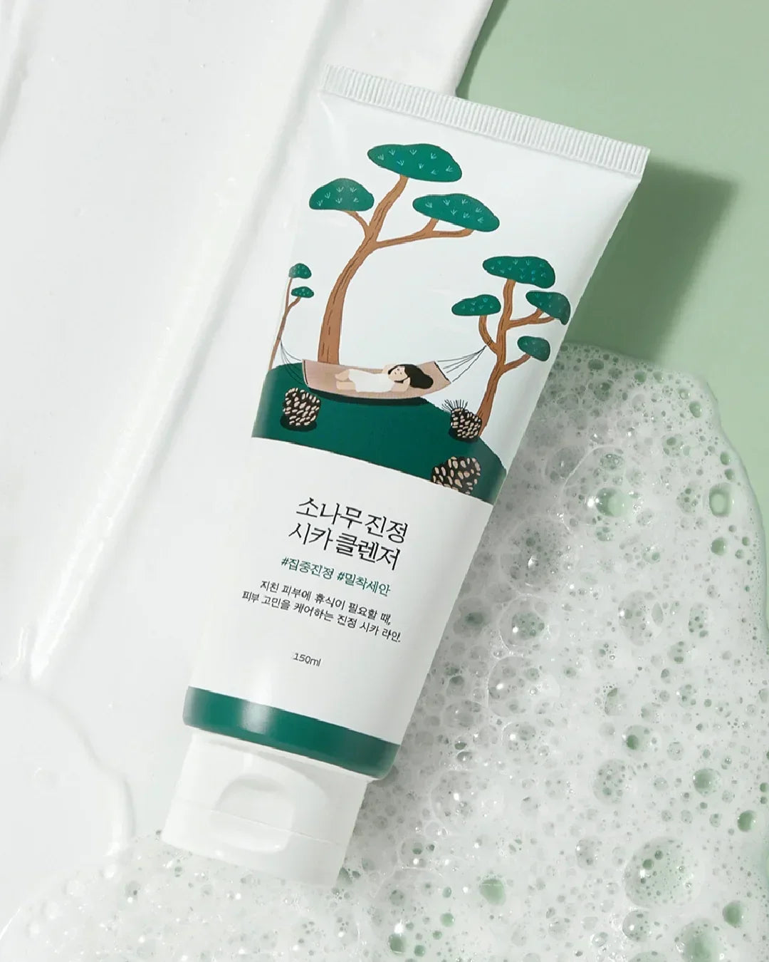 Pine Calming Cica Cleanser tube with green tree illustration on foam-covered surface