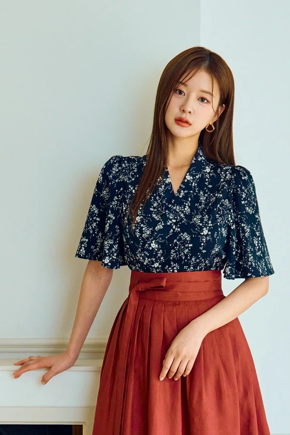 Woman wearing navy floral blouse with flutter sleeves and high-waist rust red skirt indoors