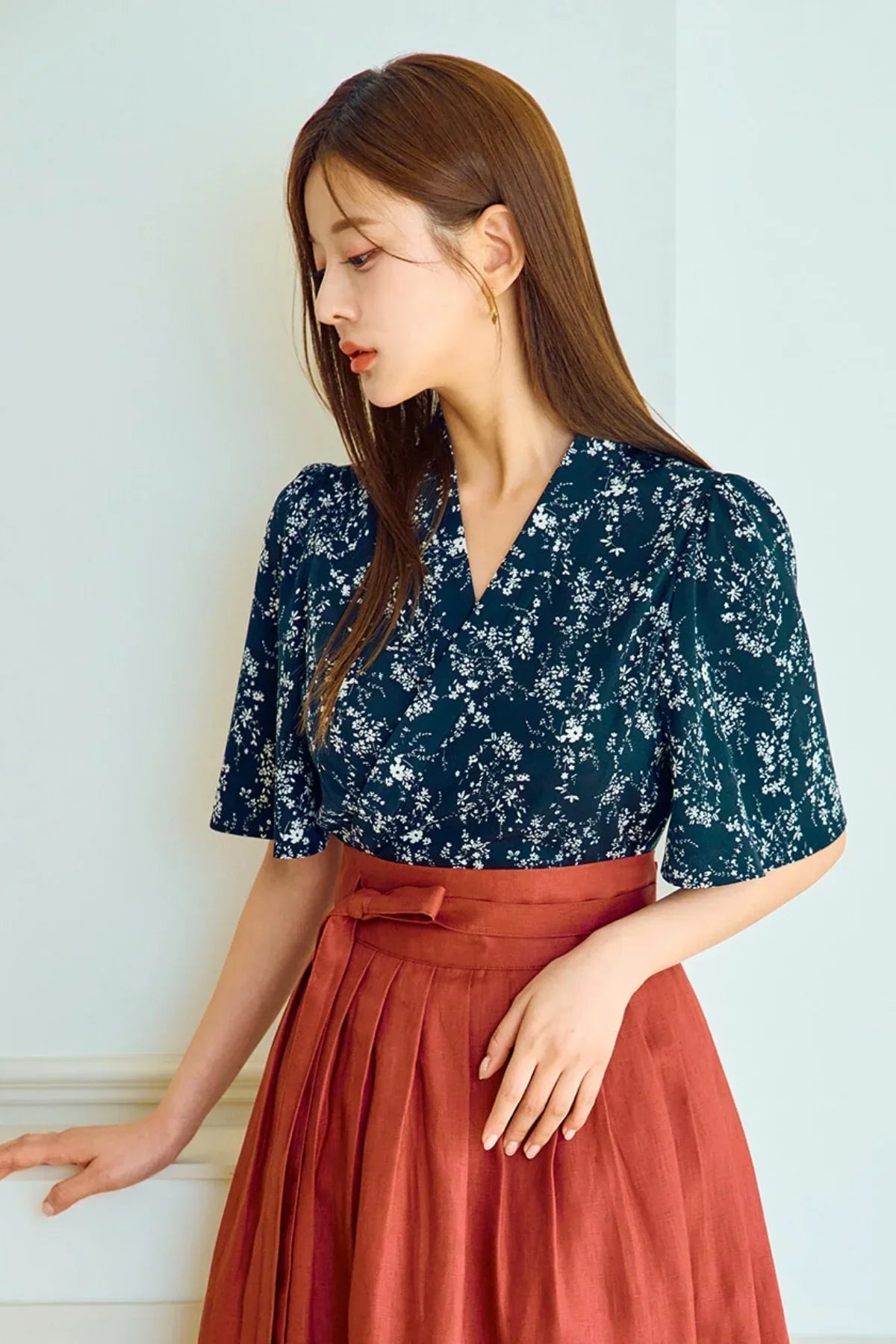 Woman in navy floral blouse and rust-colored pleated skirt standing indoors