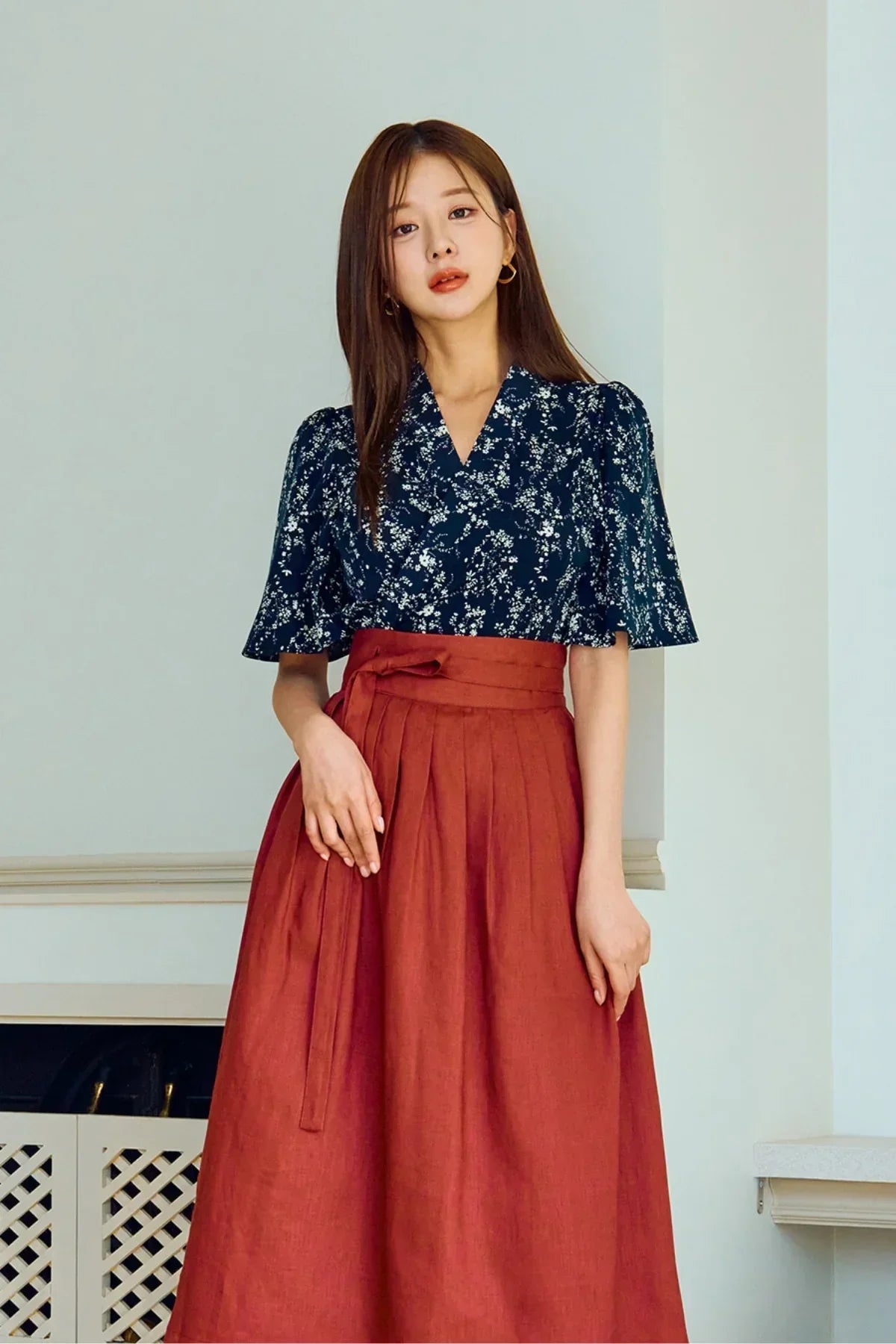 Woman wearing navy floral blouse with puff sleeves and high-waisted burnt orange skirt indoors