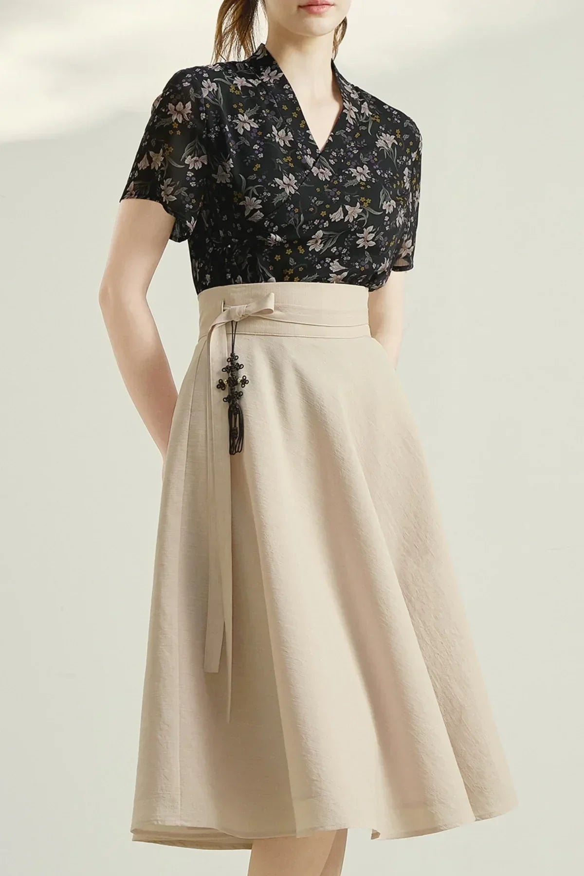 Woman wearing black floral short-sleeve blouse with beige high-waisted midi skirt featuring a tie and decorative tassel