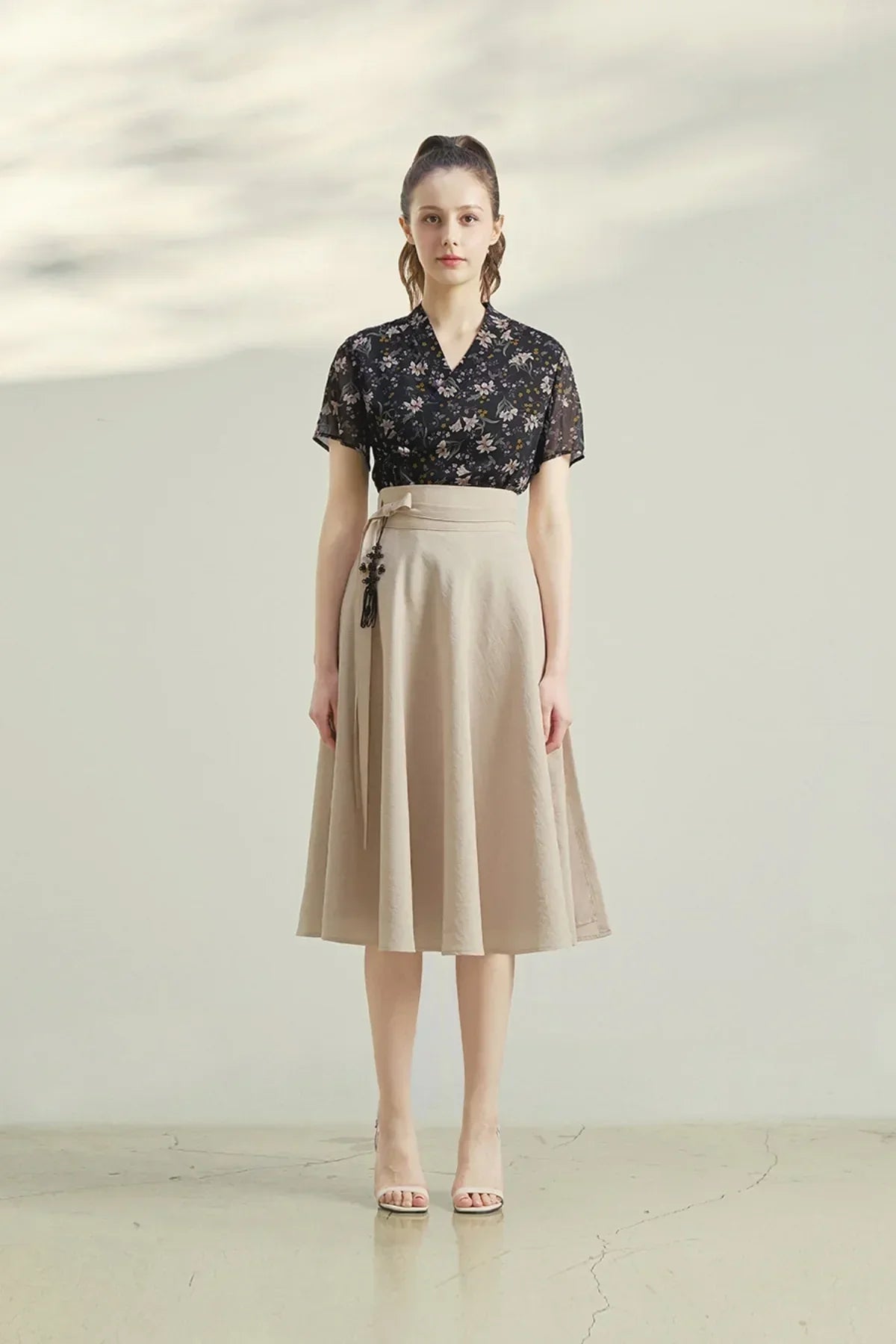 Woman wearing a beige midi wrap skirt with black floral short-sleeve blouse and beige heels