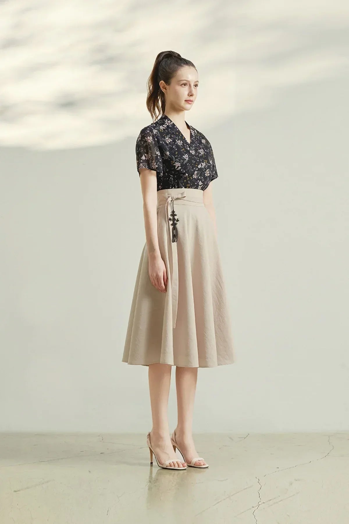 woman wearing black floral blouse and beige midi skirt with tassel belt posing indoors