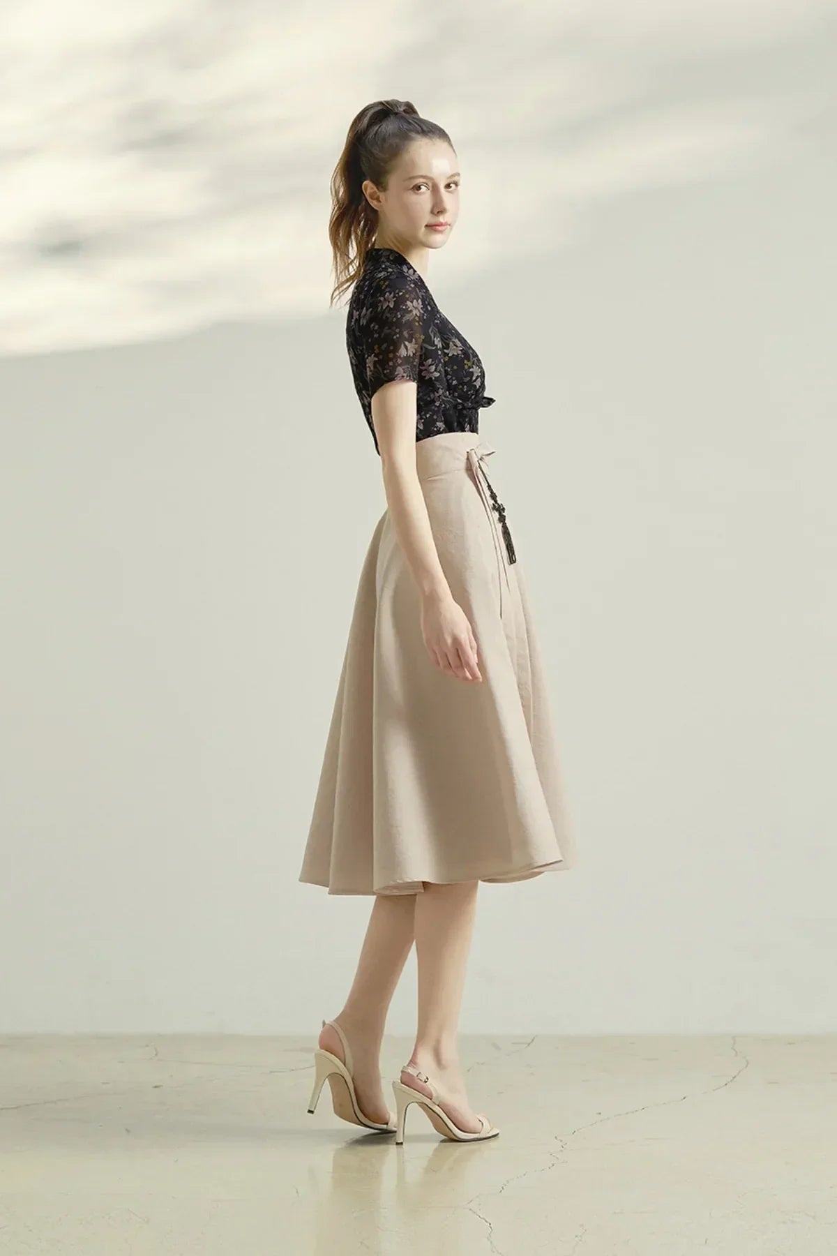 woman wearing floral black top and beige high-waisted midi skirt posing in minimalist studio