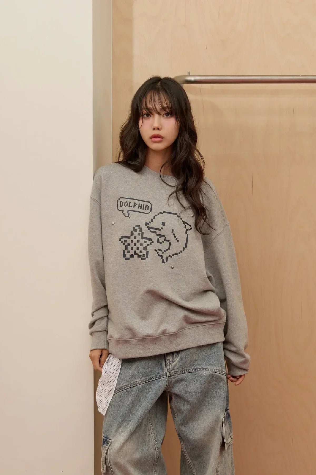 young woman wearing grey sweatshirt with pixel dolphin and star graphic, paired with baggy jeans