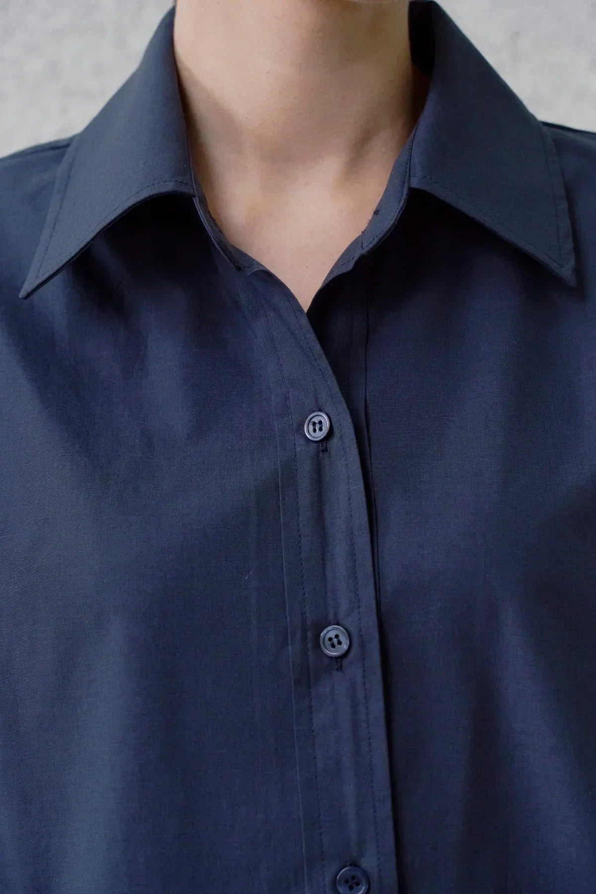 Close-up of a navy blue poplin shirt with buttons and a pointed collar on a person