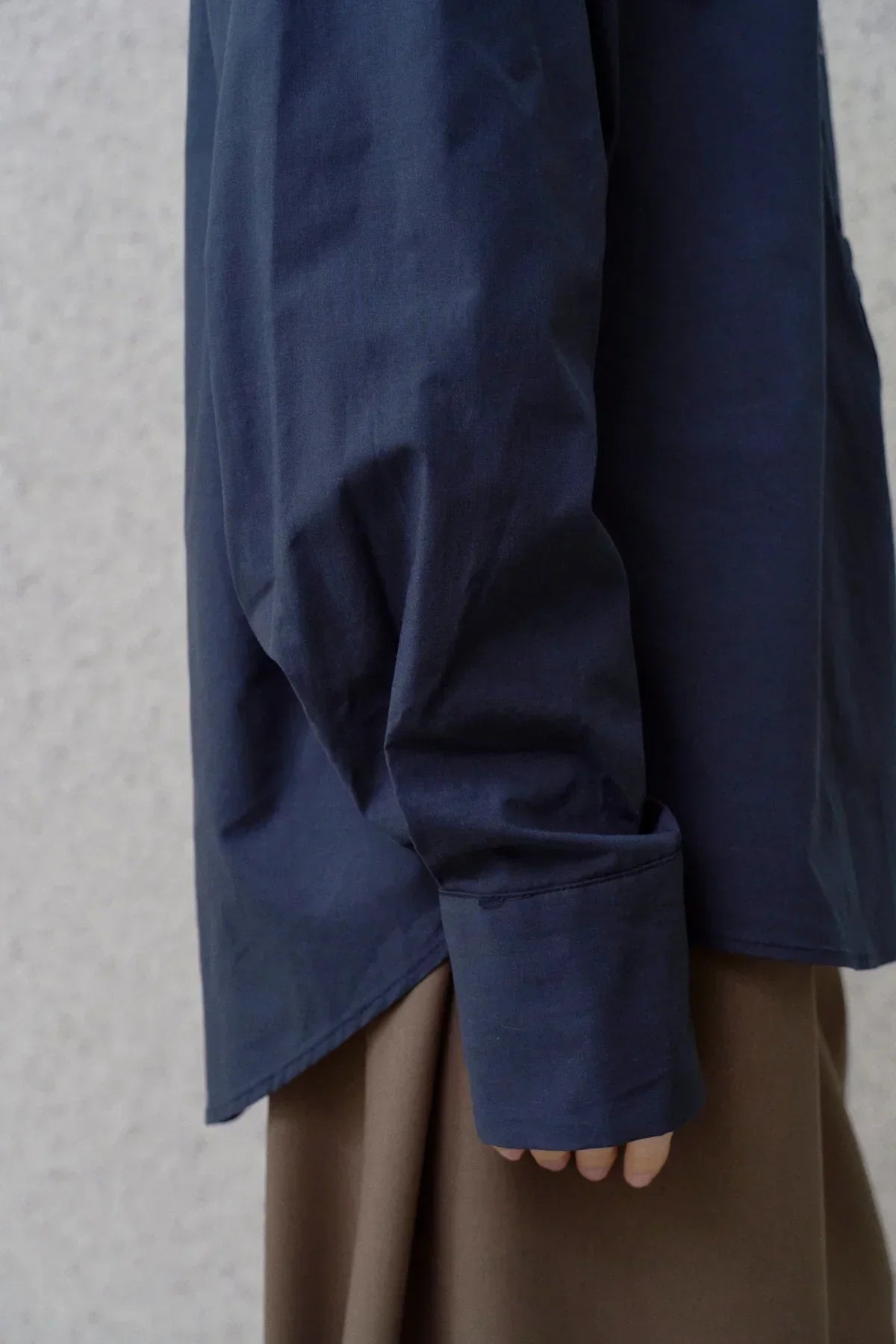 Close-up of navy poplin shirt sleeve with buttoned cuff over brown skirt