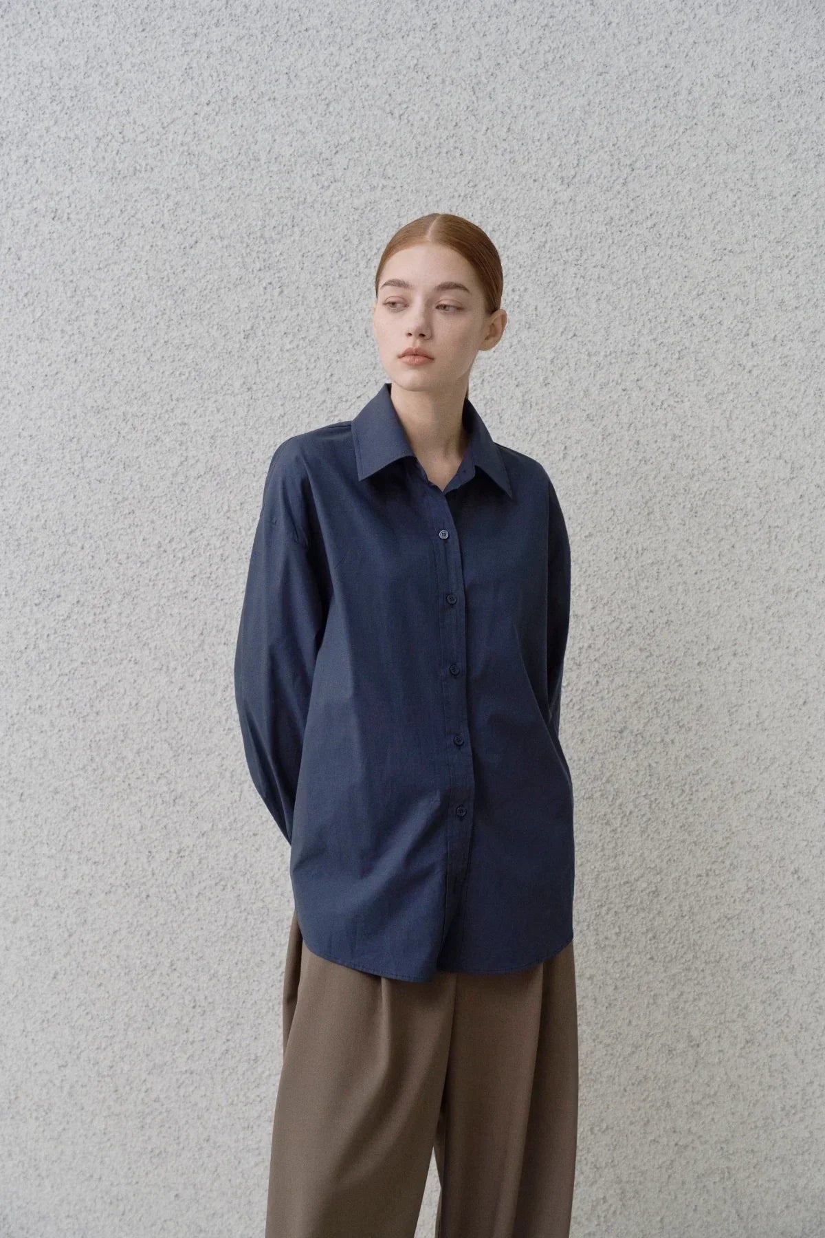 Woman wearing a navy blue poplin button-up shirt with brown wide-leg pants against a textured gray wall