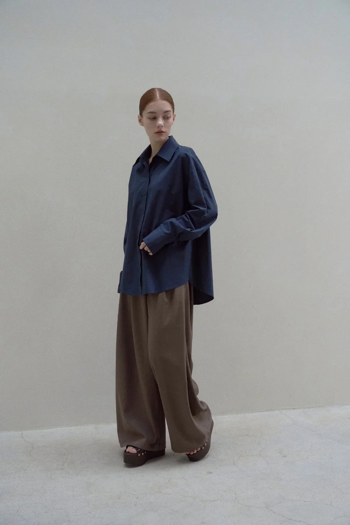 Model wearing navy oversized poplin shirt and wide brown pants on neutral background