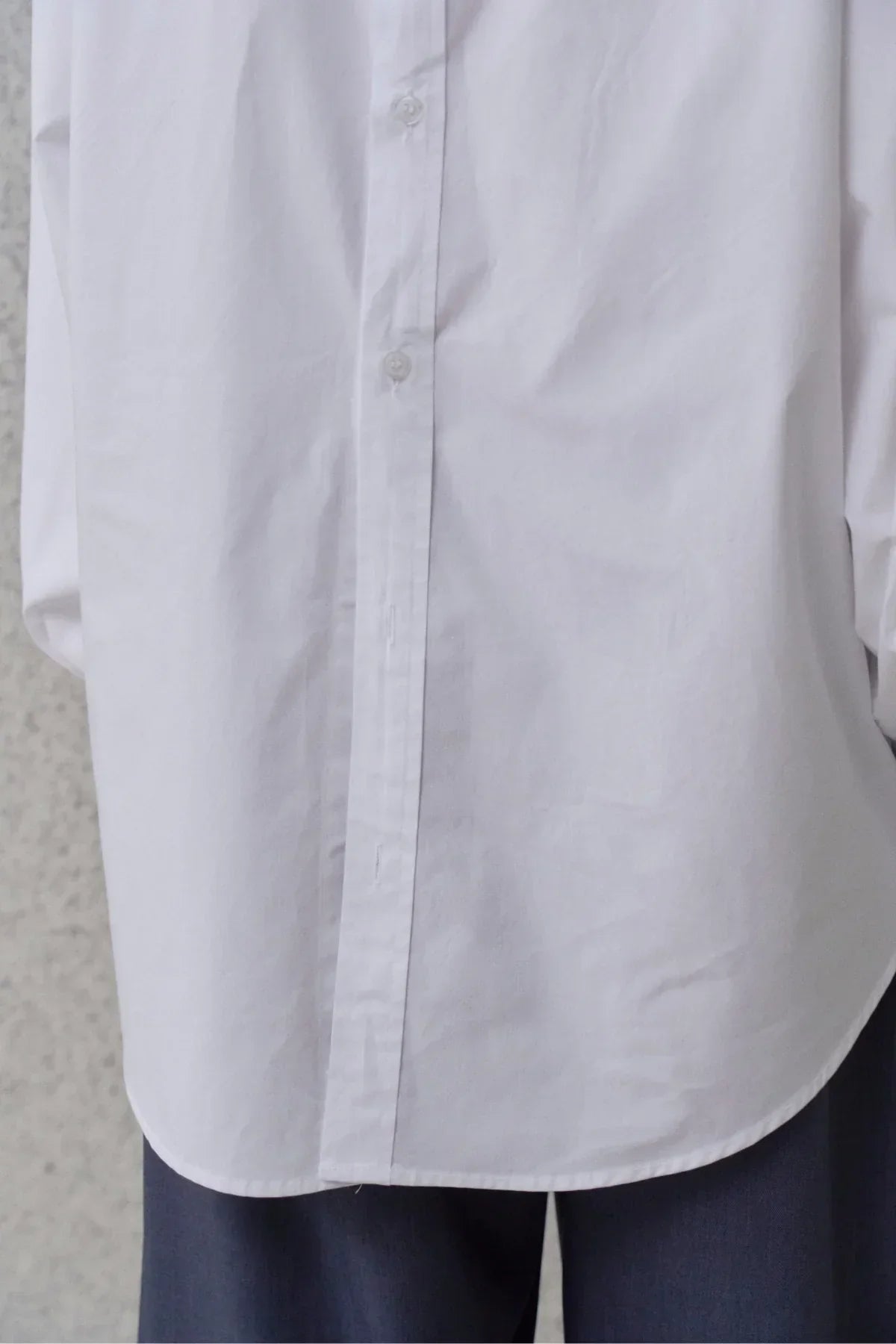 Close-up of white poplin button-down shirt and dark trousers on person against textured background