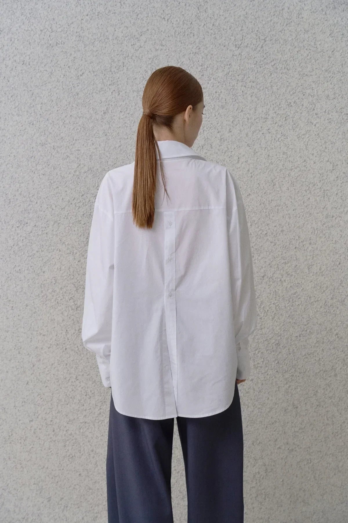 Back view of woman wearing white poplin button-back shirt with long sleeves and navy pants