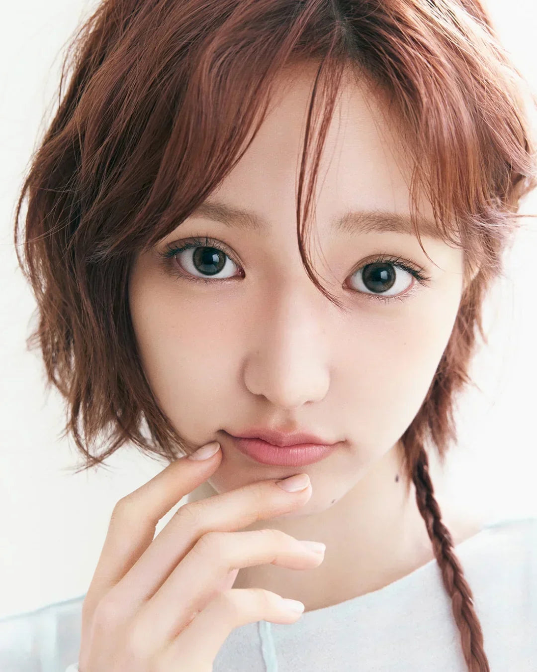 Close-up portrait of a young woman with short brown hair and a braided strand, clear skin, and natural makeup