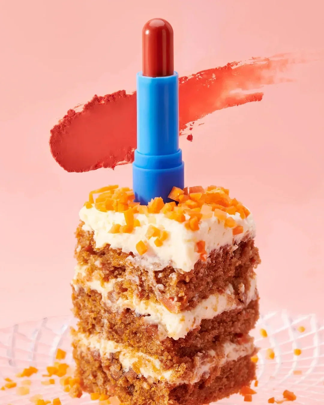 Blue lip balm with red tint standing on a slice of carrot cake with cream and carrot pieces