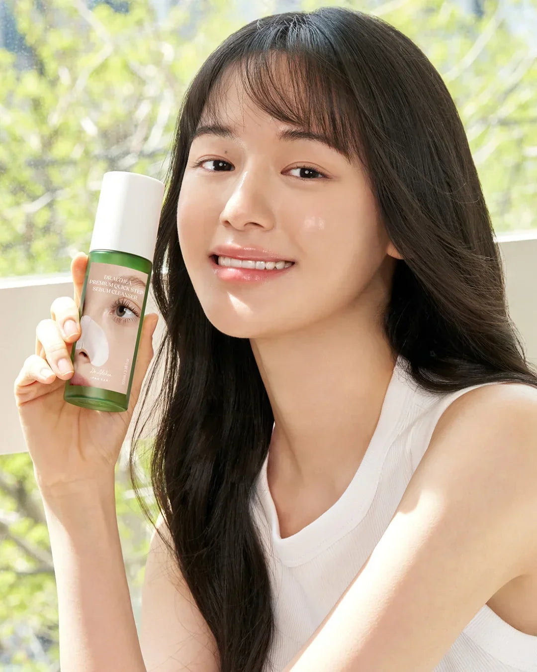 Smiling woman holding Dr. Althea Premium Quick Step Sebum Cleanser bottle in bright natural light