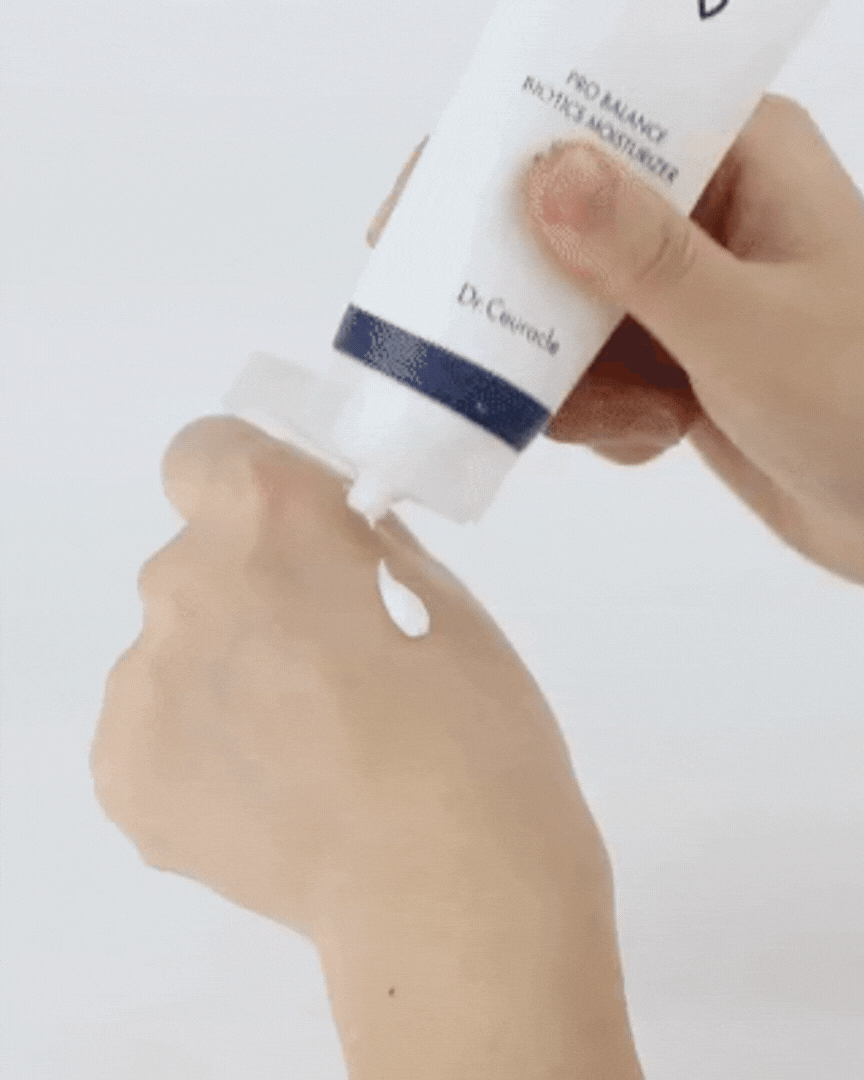 Hand squeezing white Pro Balance Biotics Moisturizer from tube onto skin against white background