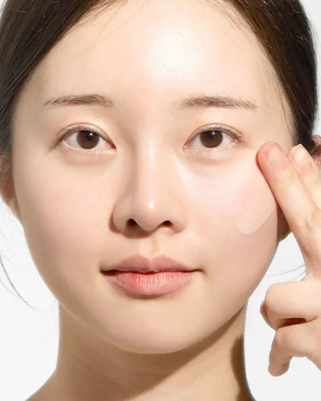 Close-up of woman applying translucent skincare product to cheek for radiant skin