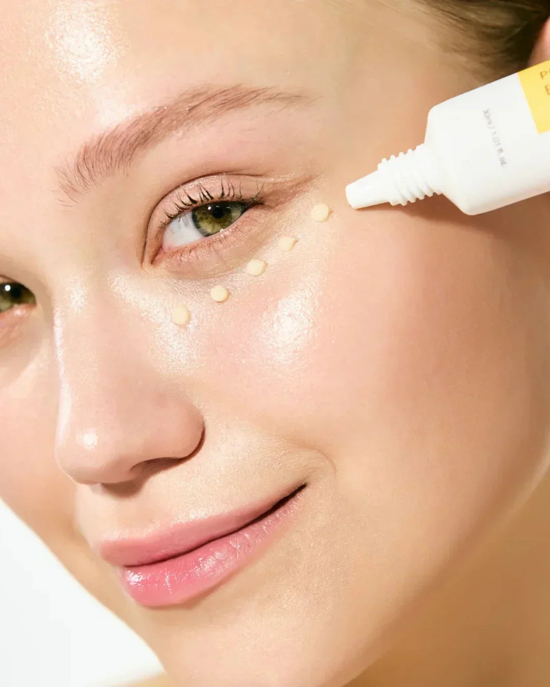 Close-up of woman applying propolis vitamin eye cream dots under eye for skincare