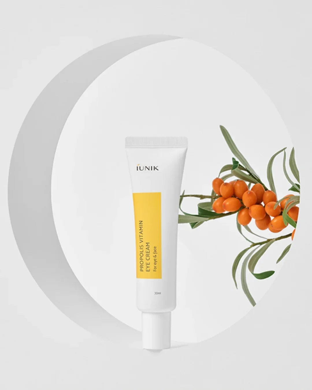 iUNIK Propolis Vitamin Eye Cream tube with sea buckthorn branch on white circular background