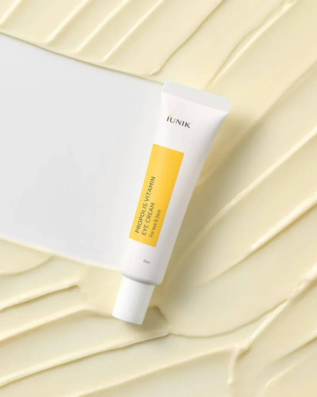iUNIK Propolis Vitamin Eye Cream tube on a textured creamy yellow background, 30ml skincare