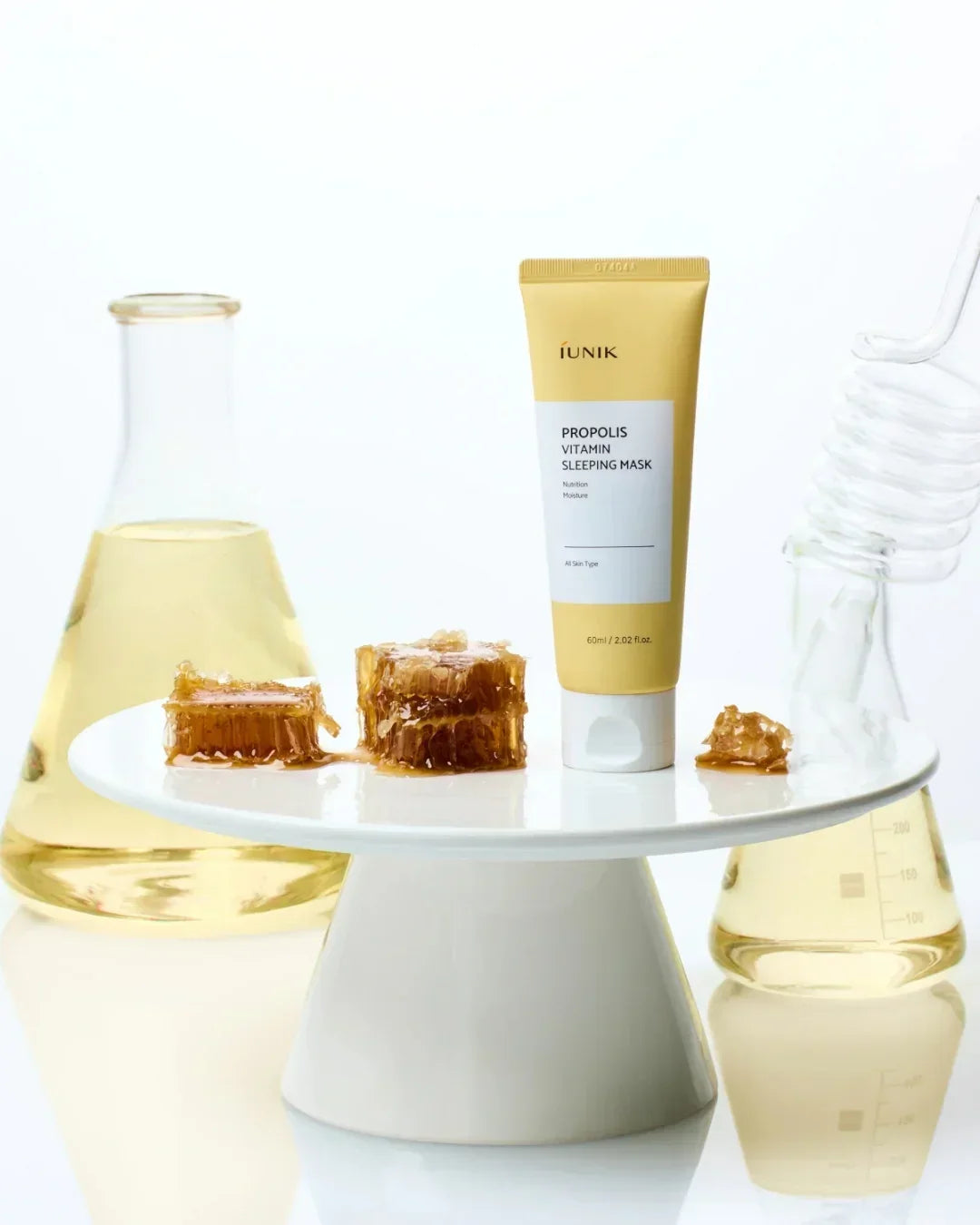 IUNIK Propolis Vitamin Sleeping Mask with honeycomb pieces on white stand and glass beakers of liquid