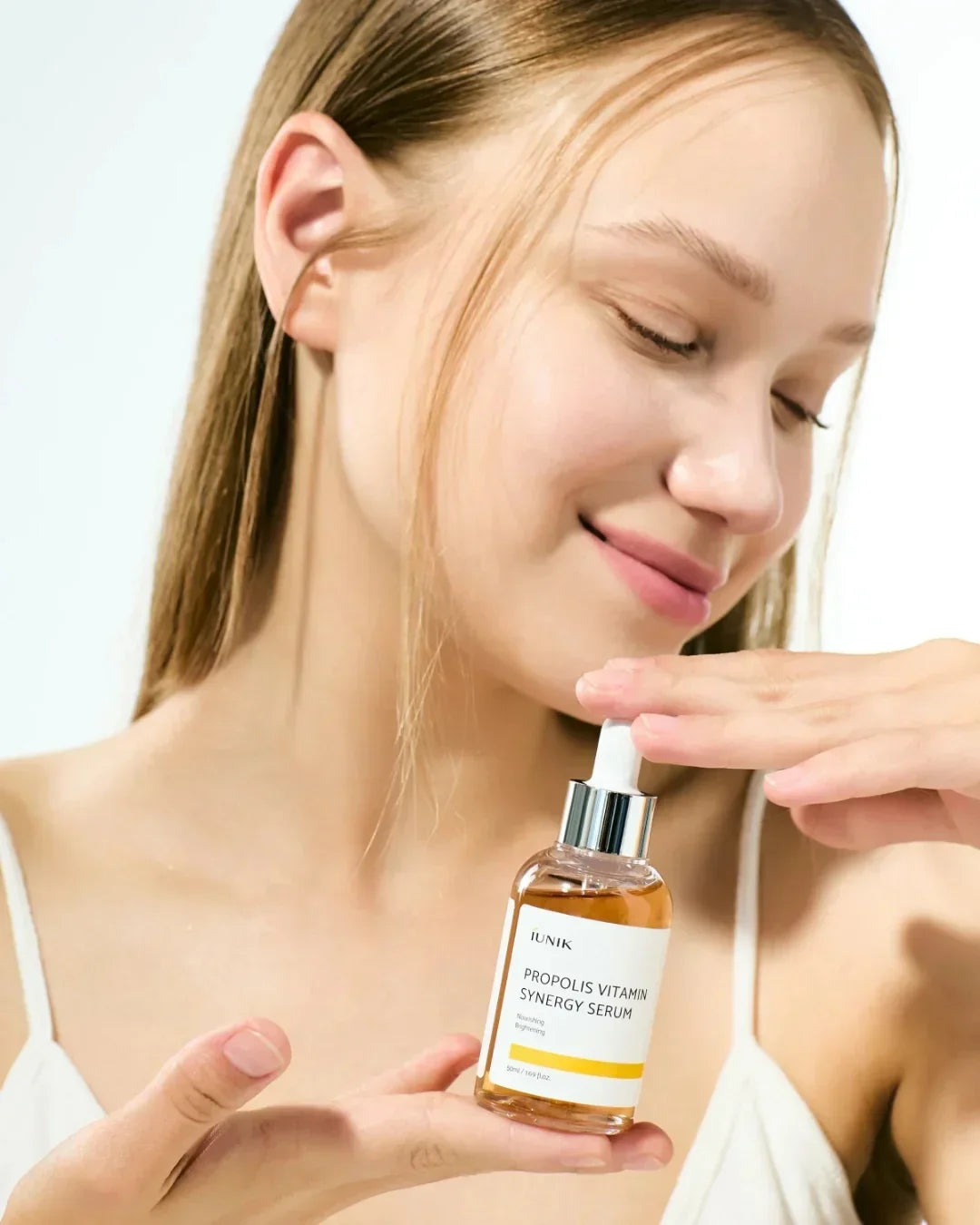 Woman holding IUNIK Propolis Vitamin Synergy Serum skincare bottle with dropper, radiant clear skin