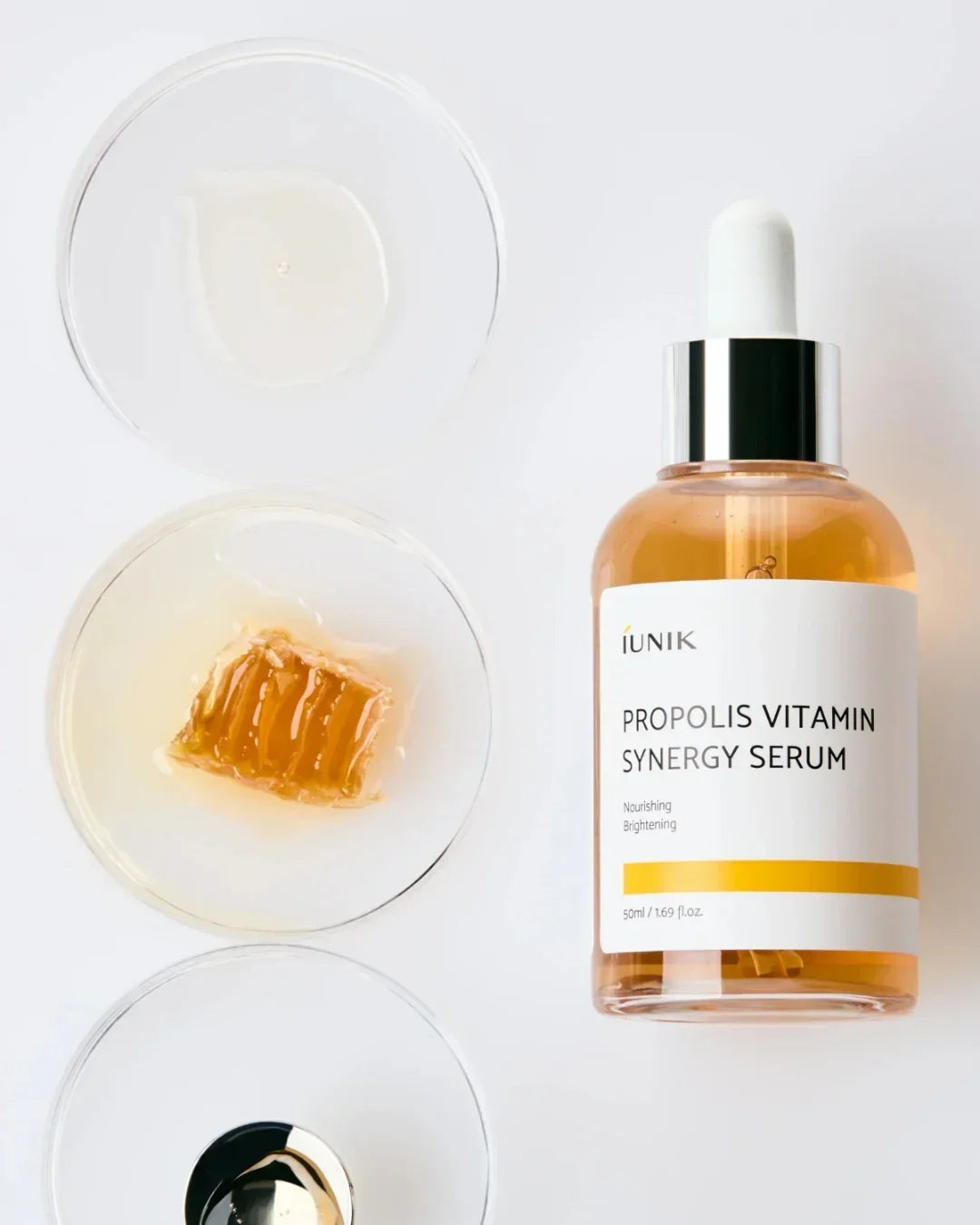 iUNIK Propolis Vitamin Synergy Serum bottle with dropper alongside honeycomb and serum samples on clear dishes