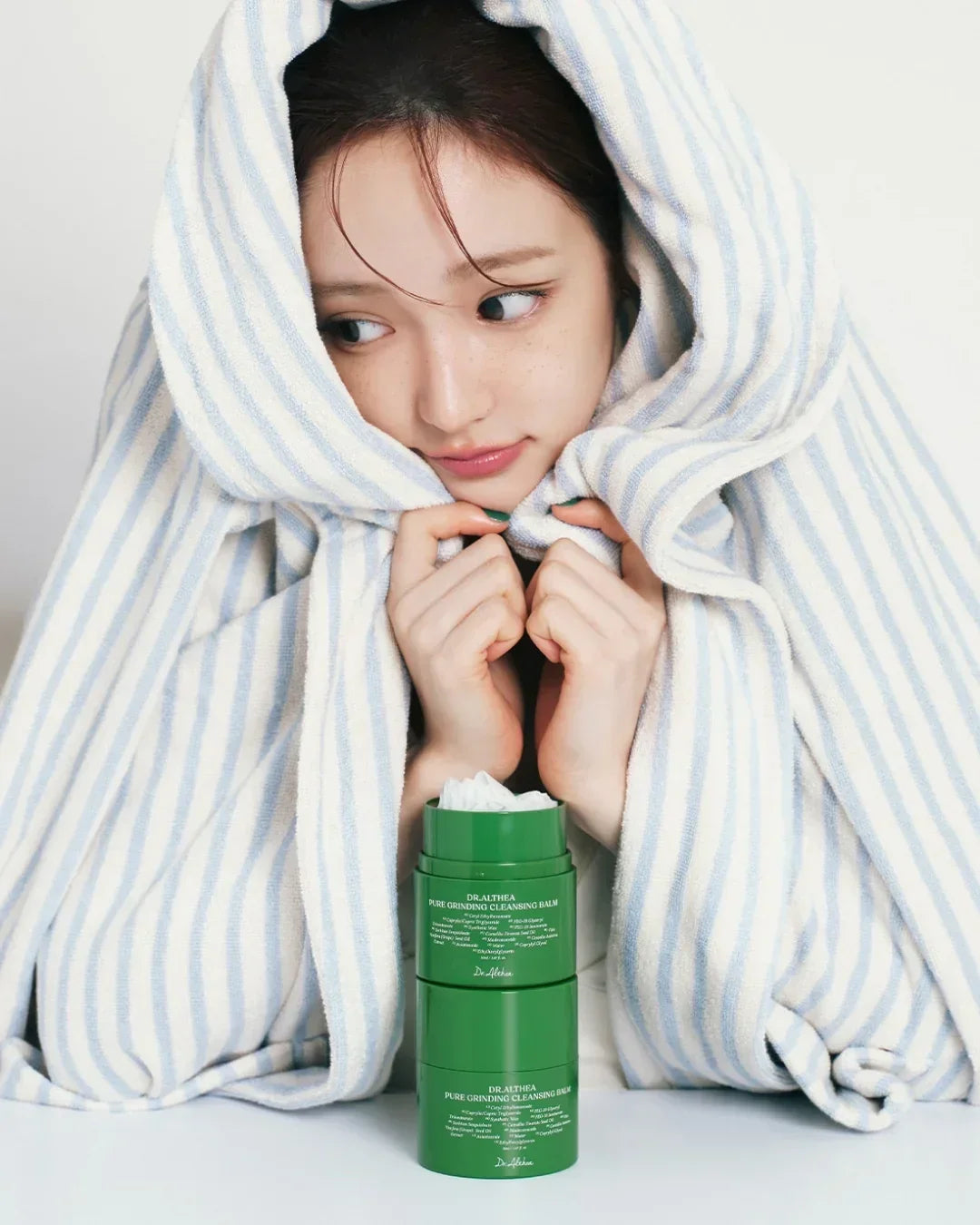 Young woman wrapped in striped towel with Dr.Althea Pure Grinding Cleansing Balm container