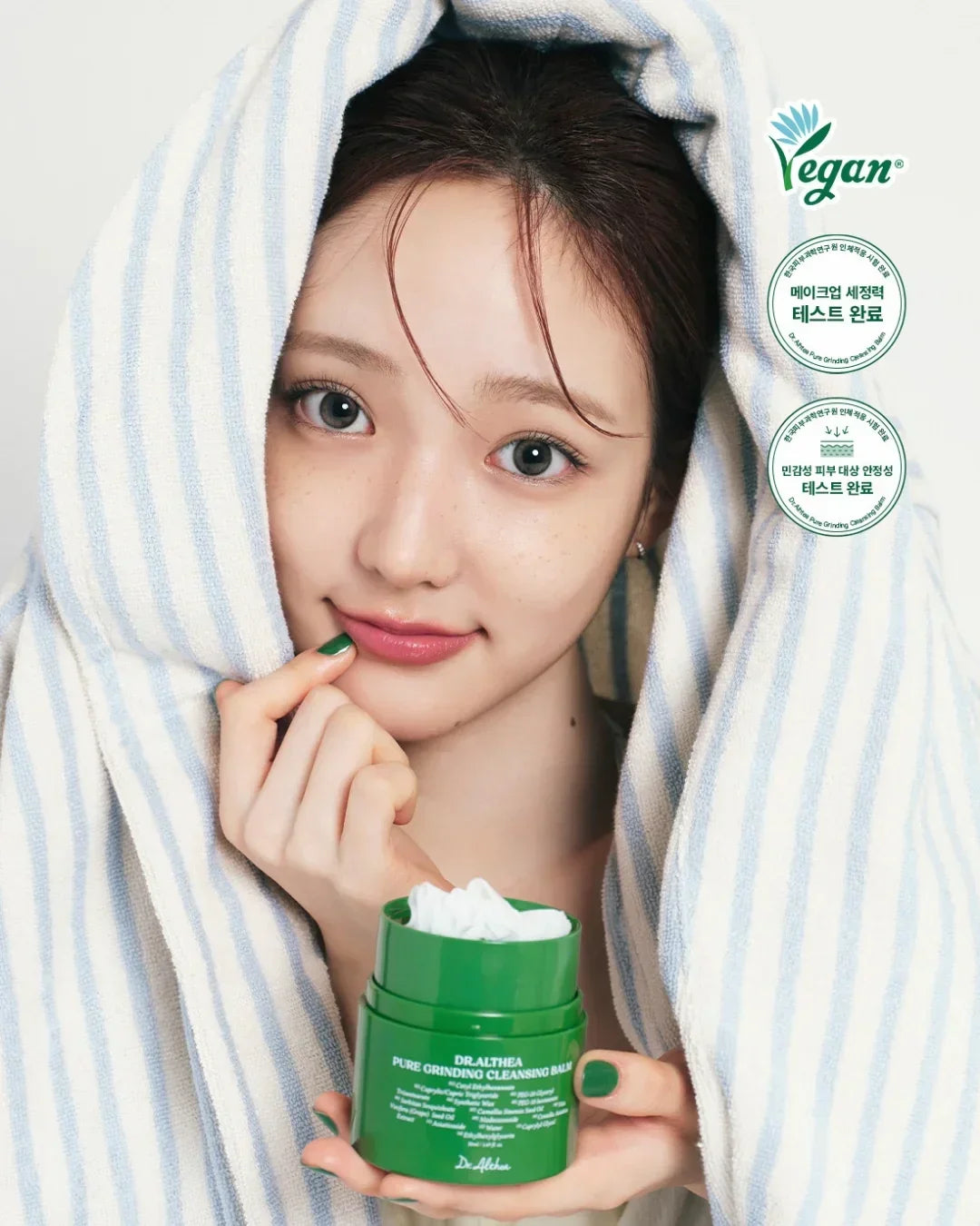 Young woman with fresh skin wrapped in striped towel holding Dr.Althea Pure Grinding Cleansing Balm green jar