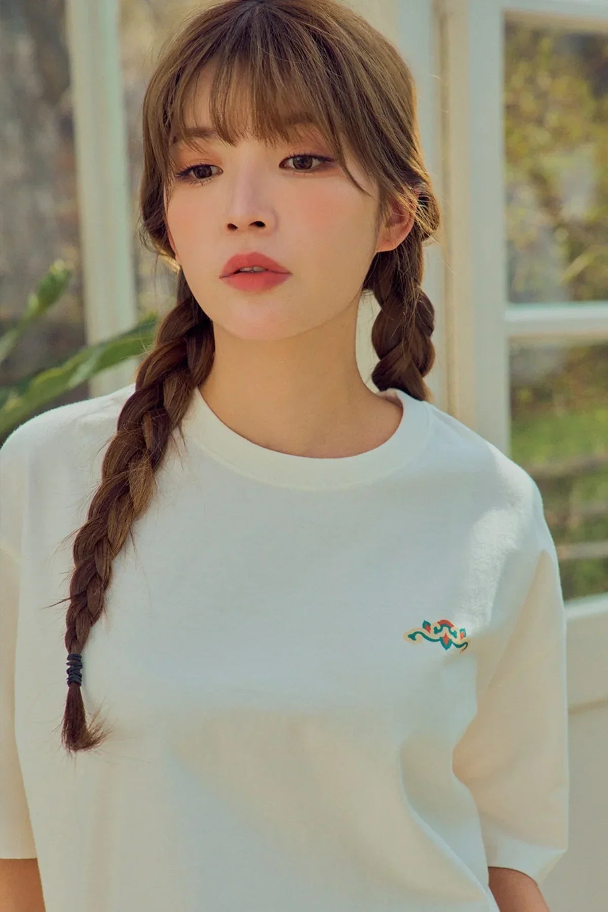 Young woman wearing white t-shirt with small colorful design, braided hair, indoor natural light