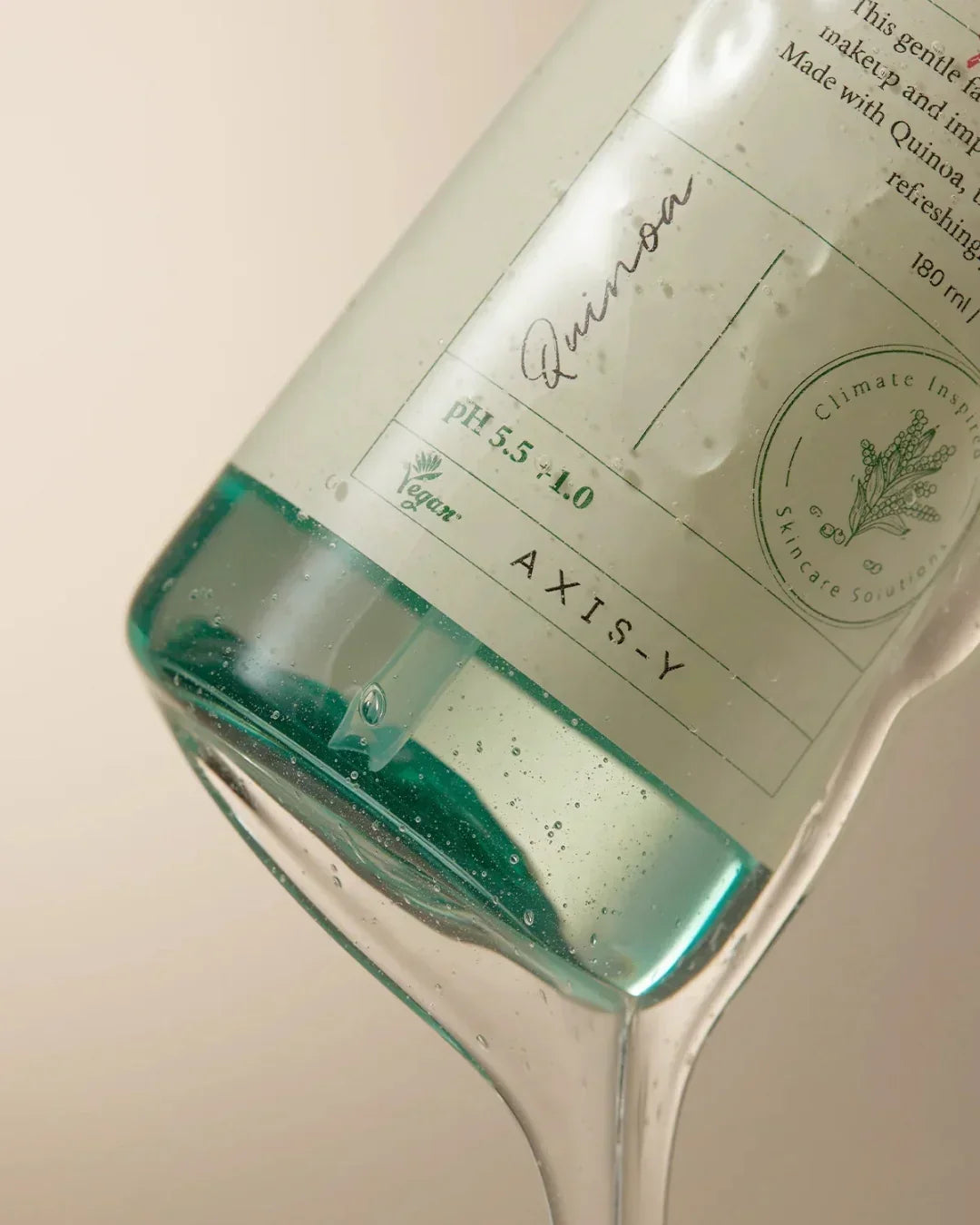 Close-up of Axis-Y Quinoa One Step Balanced Gel Cleanser bottle with clear gel and water droplets