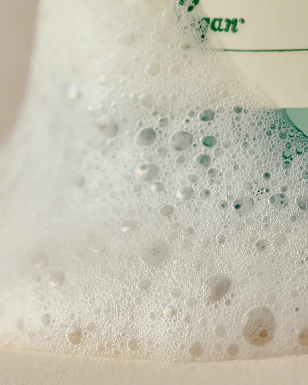 Foamy bubbles on a surface partially covering a Quinoa One Step Balanced Gel Cleanser bottle