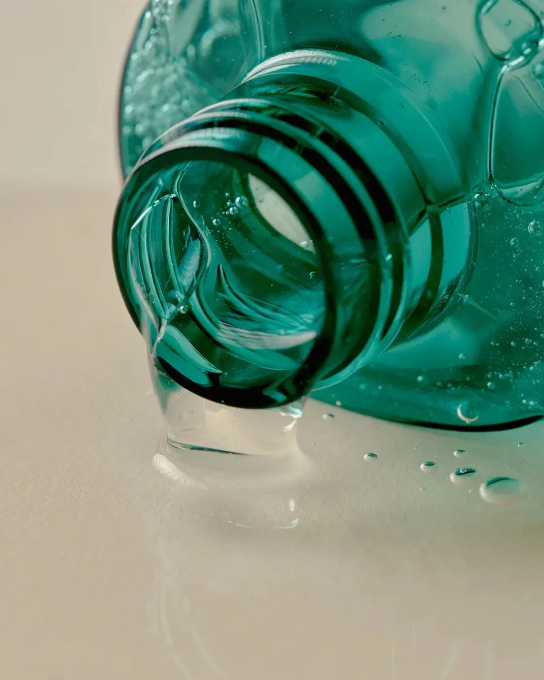 Close-up of clear gel cleanser pouring from green bottle on beige surface