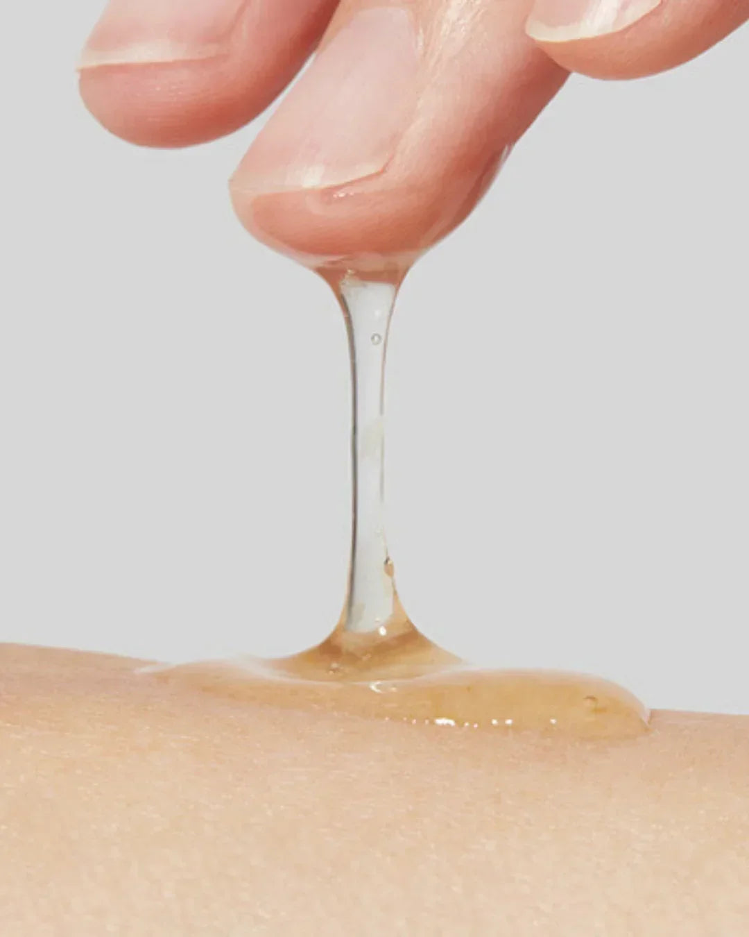 Close-up of a finger pulling up clear, sticky calendula peel-off mask gel from skin