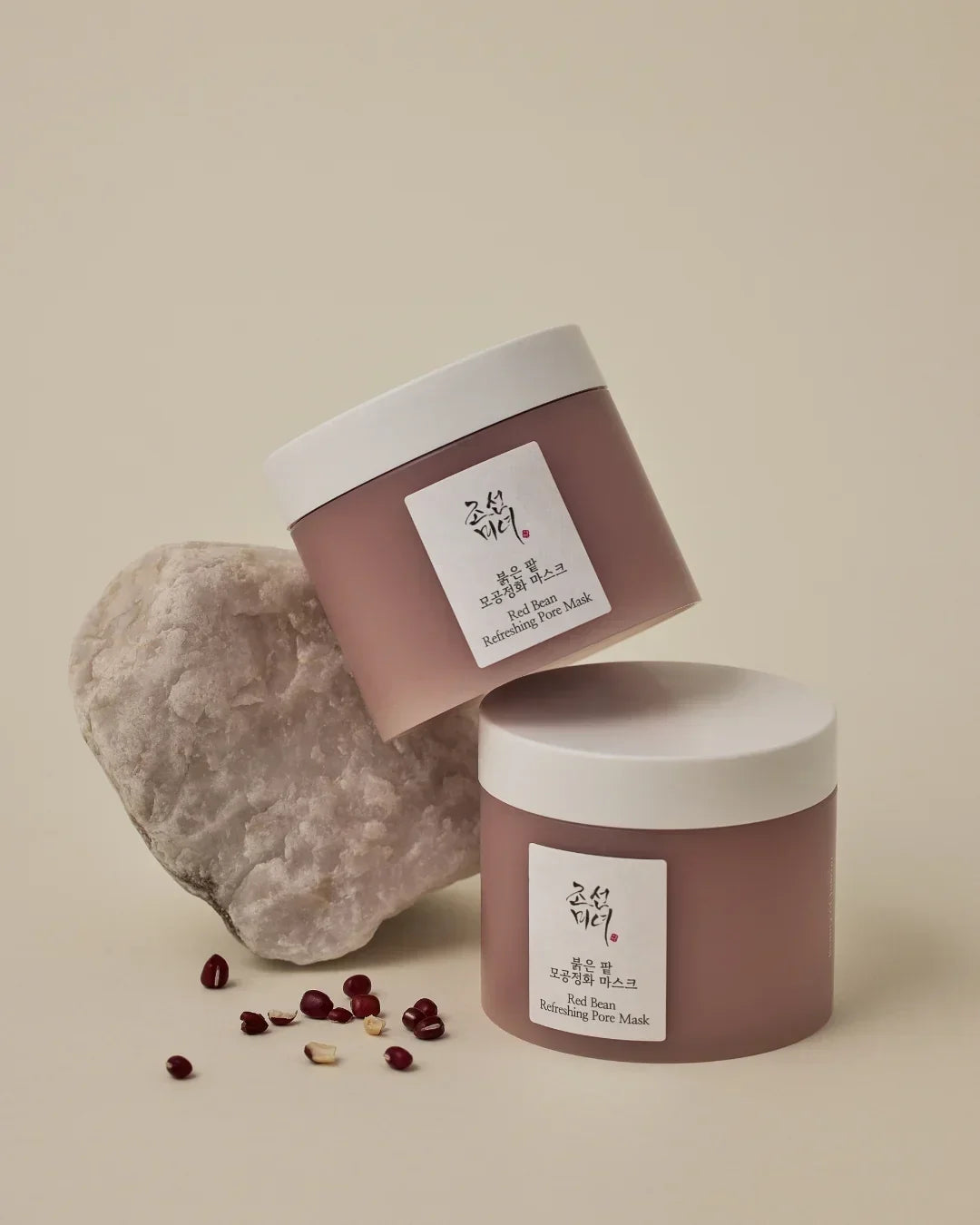 Two jars of Red Bean Refreshing Pore Mask with white lids, red beans, and a textured stone on beige background