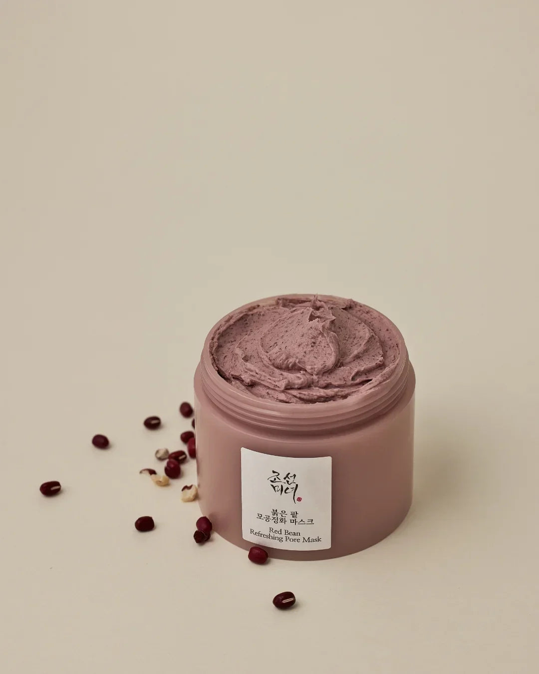 Open jar of red bean refreshing pore mask cream with scattered red beans on beige background
