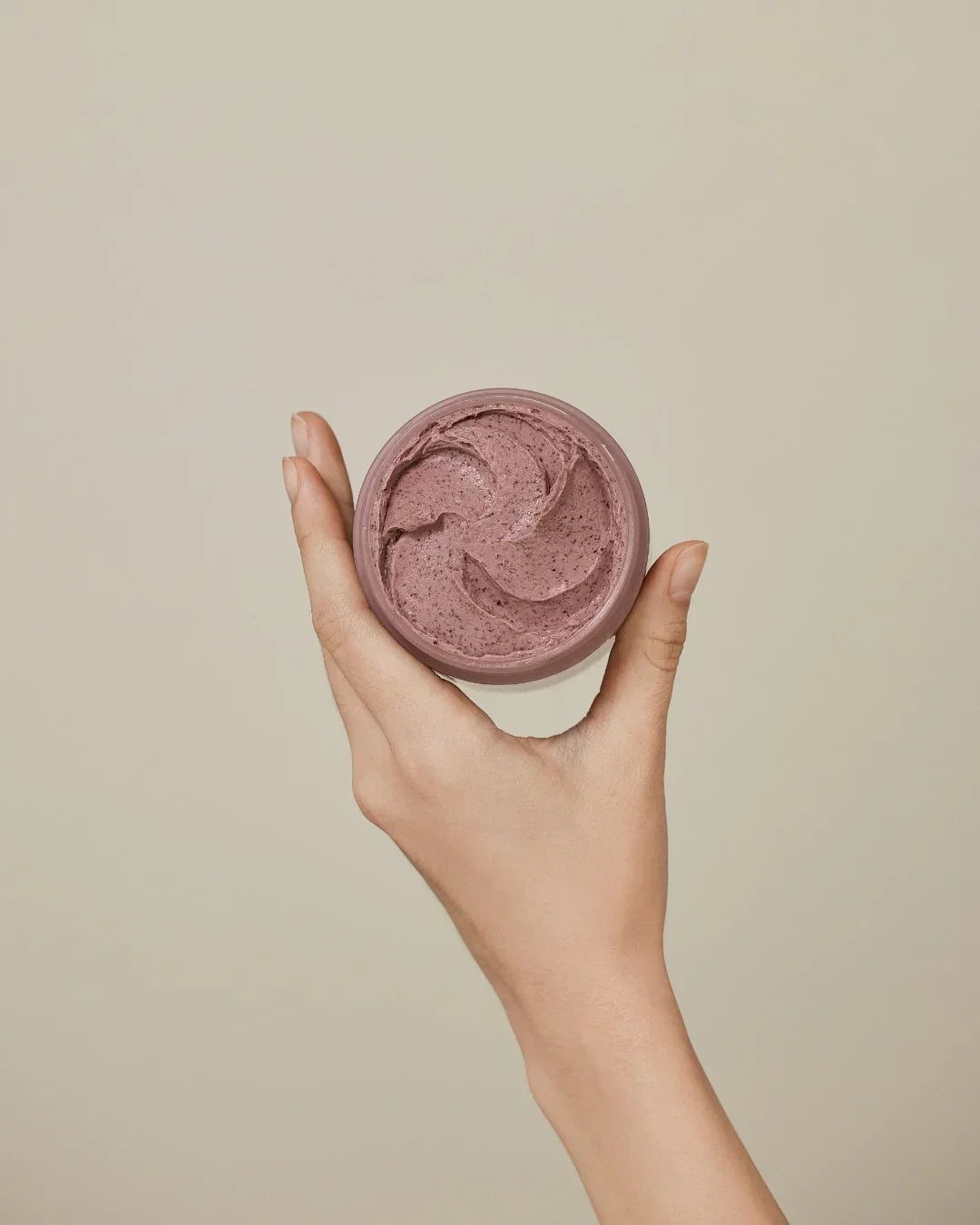 Hand holding open jar of red bean refreshing pore mask with creamy texture on beige background