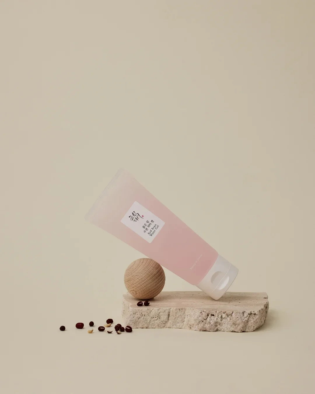 Pink Red Bean Water Gel tube balanced on wooden ball on stone slab with scattered red beans