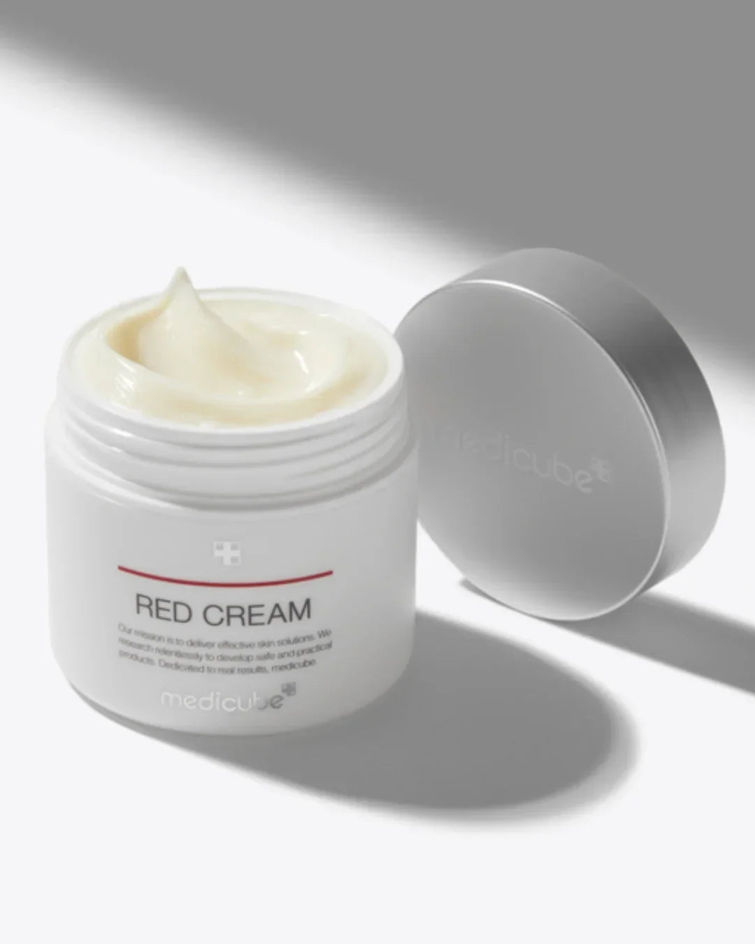 Open jar of Medicube Red Cream with soft, creamy texture and silver lid on white background