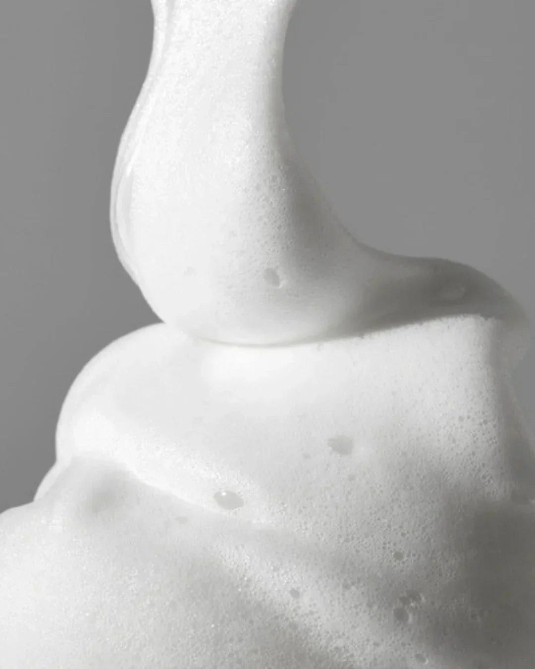 Close-up of creamy white foam texture with dense bubbles on a gray background
