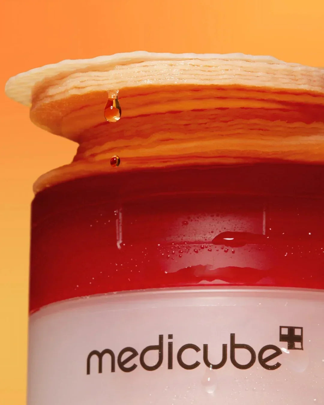 Close-up of Medicube red succinic acid peeling pad with liquid drops on orange background