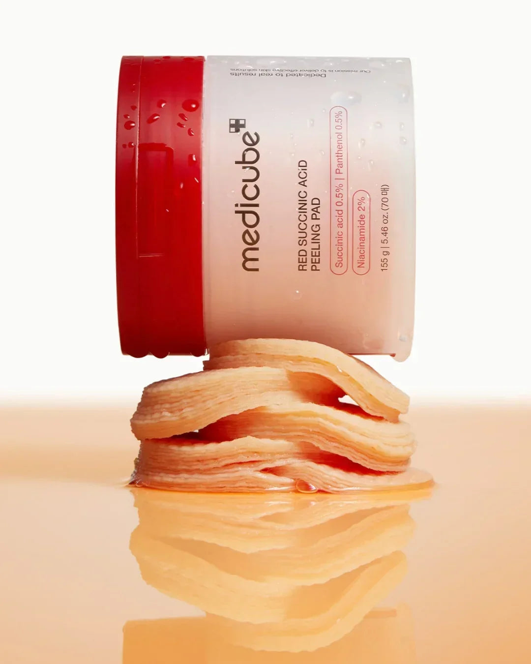 Medicube Red Succinic Acid Peeling Pad jar with stacked soaked peeling pads on reflective surface