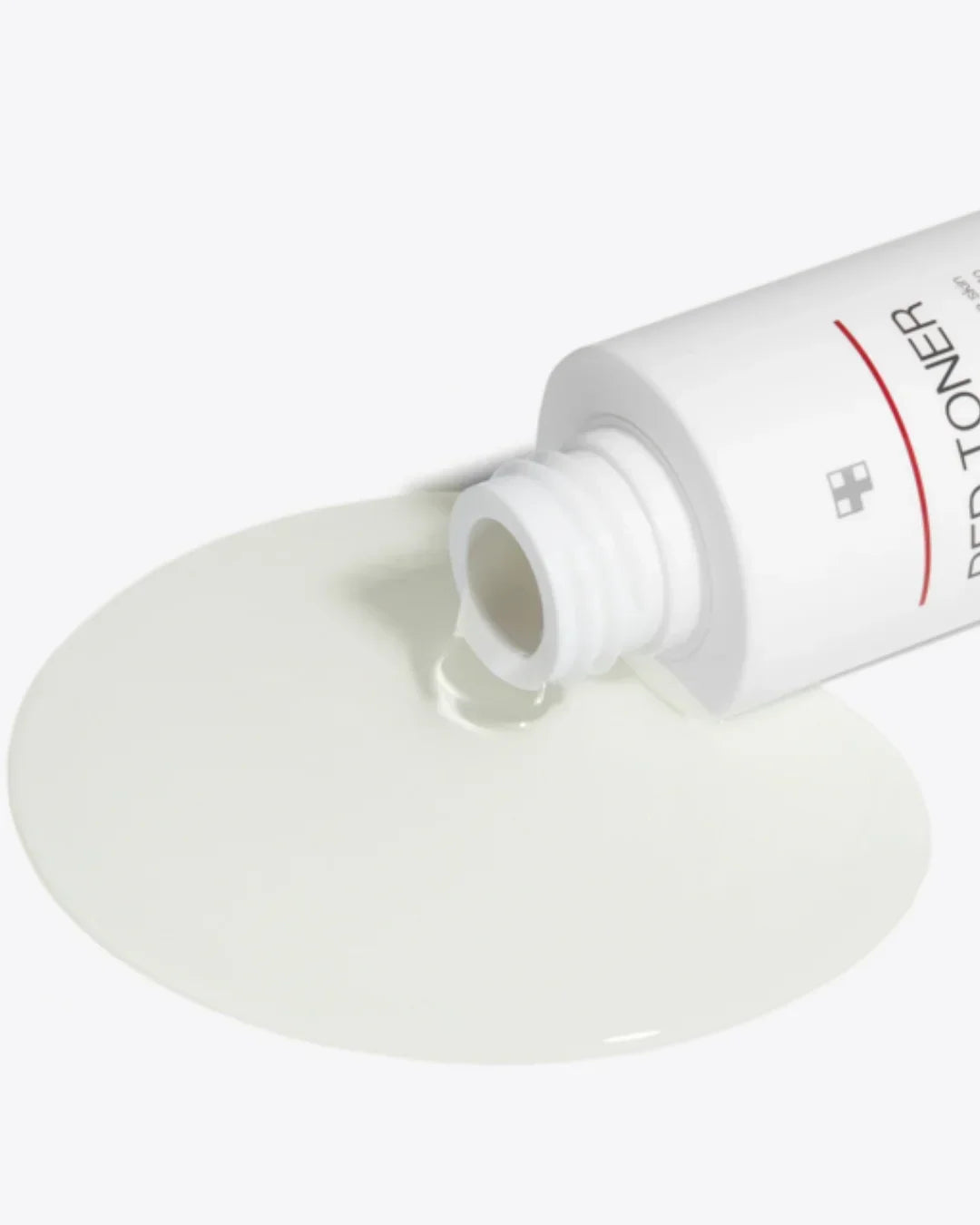 White bottle of red toner spilling clear liquid on white surface, skincare product