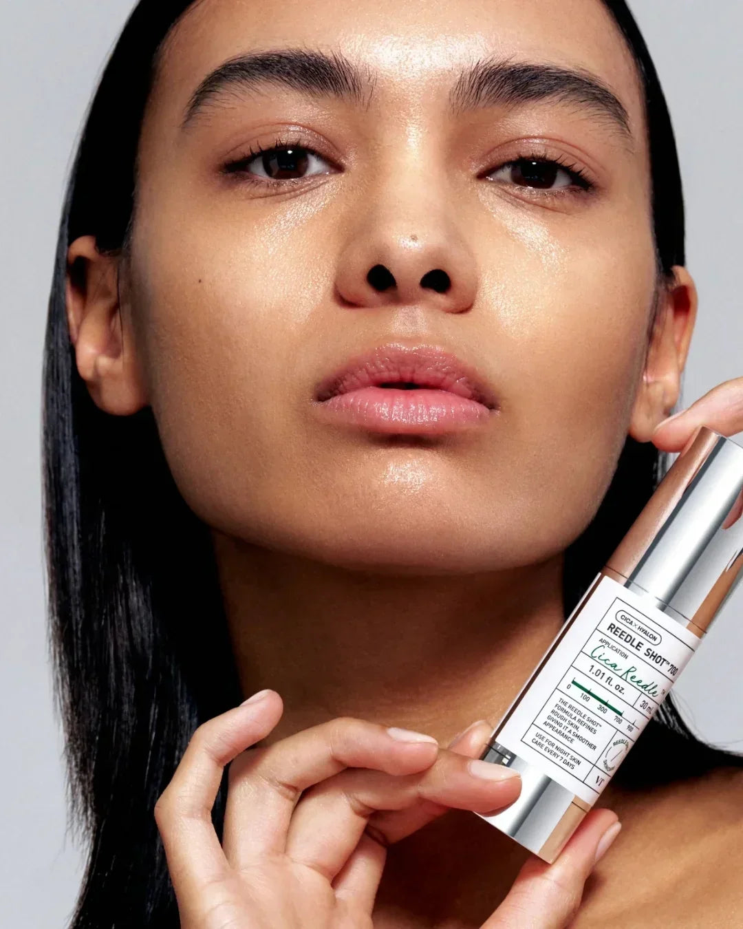 Close-up of woman with glowing skin holding Reedle Shot skincare serum bottle