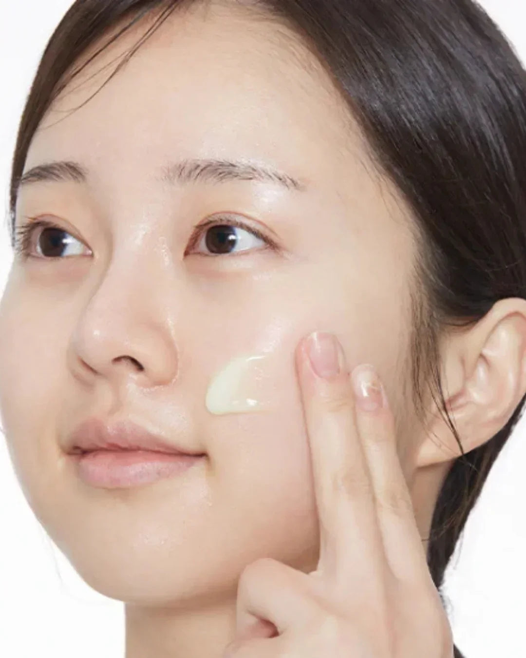 Close-up of woman applying moisturizing cream on her cheek with fingers for skincare routine