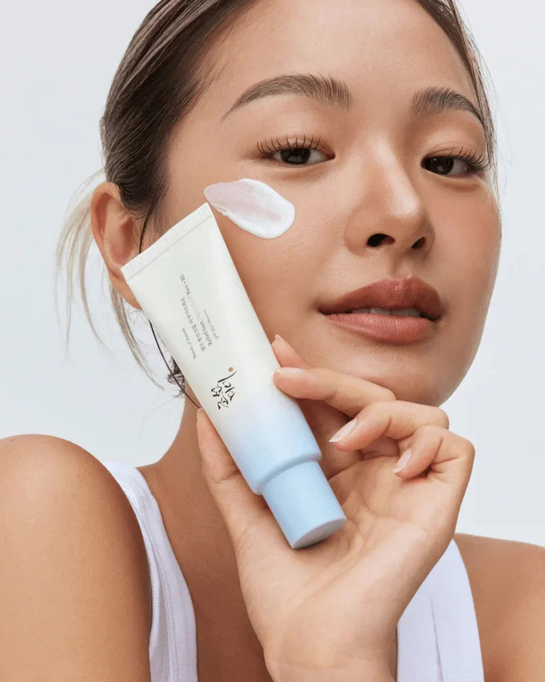 Close-up of woman applying white cream from blue and white skincare tube on cheek, clear skin makeup