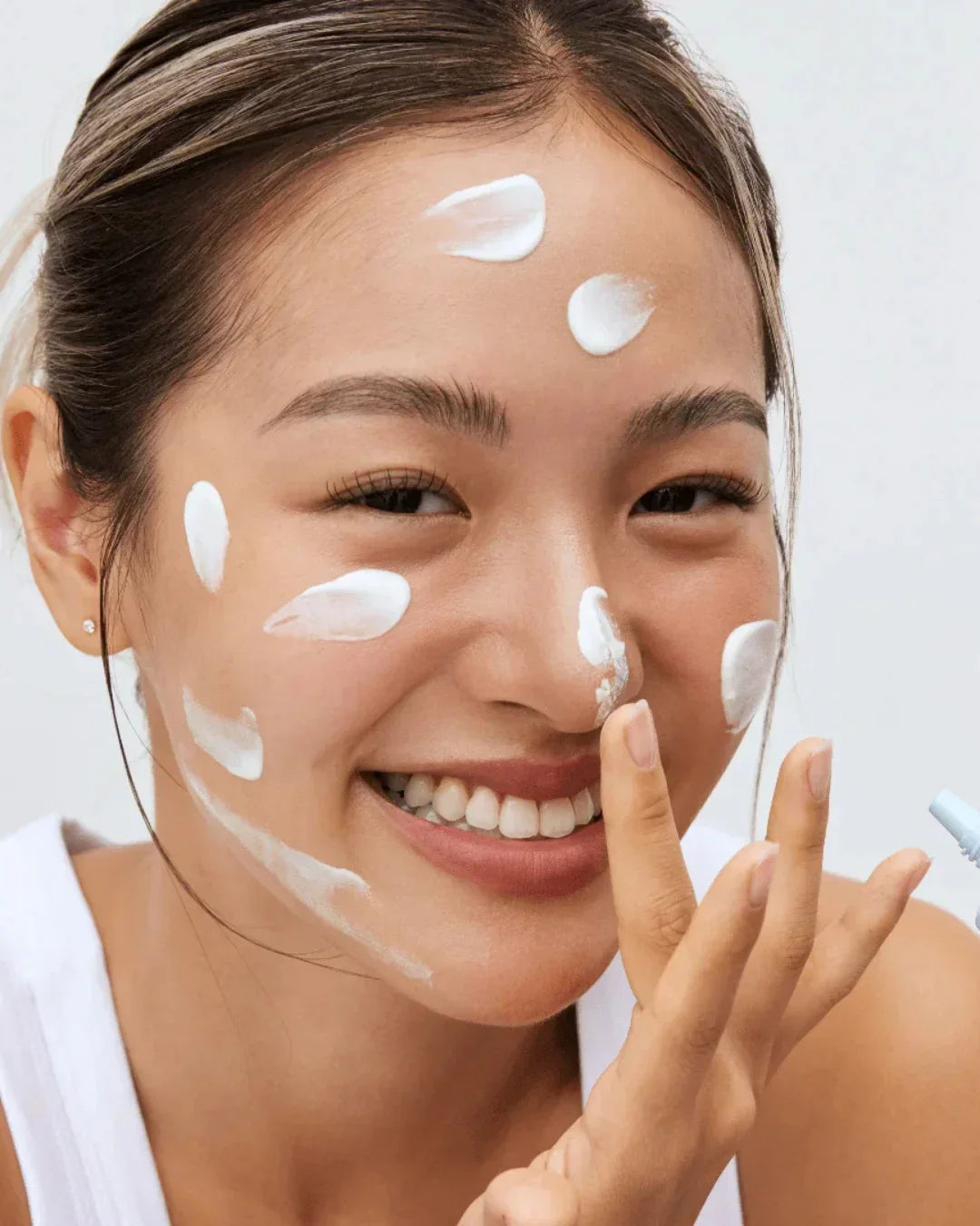 Smiling woman applying white cream dots on face, skincare routine with fresh glowing skin