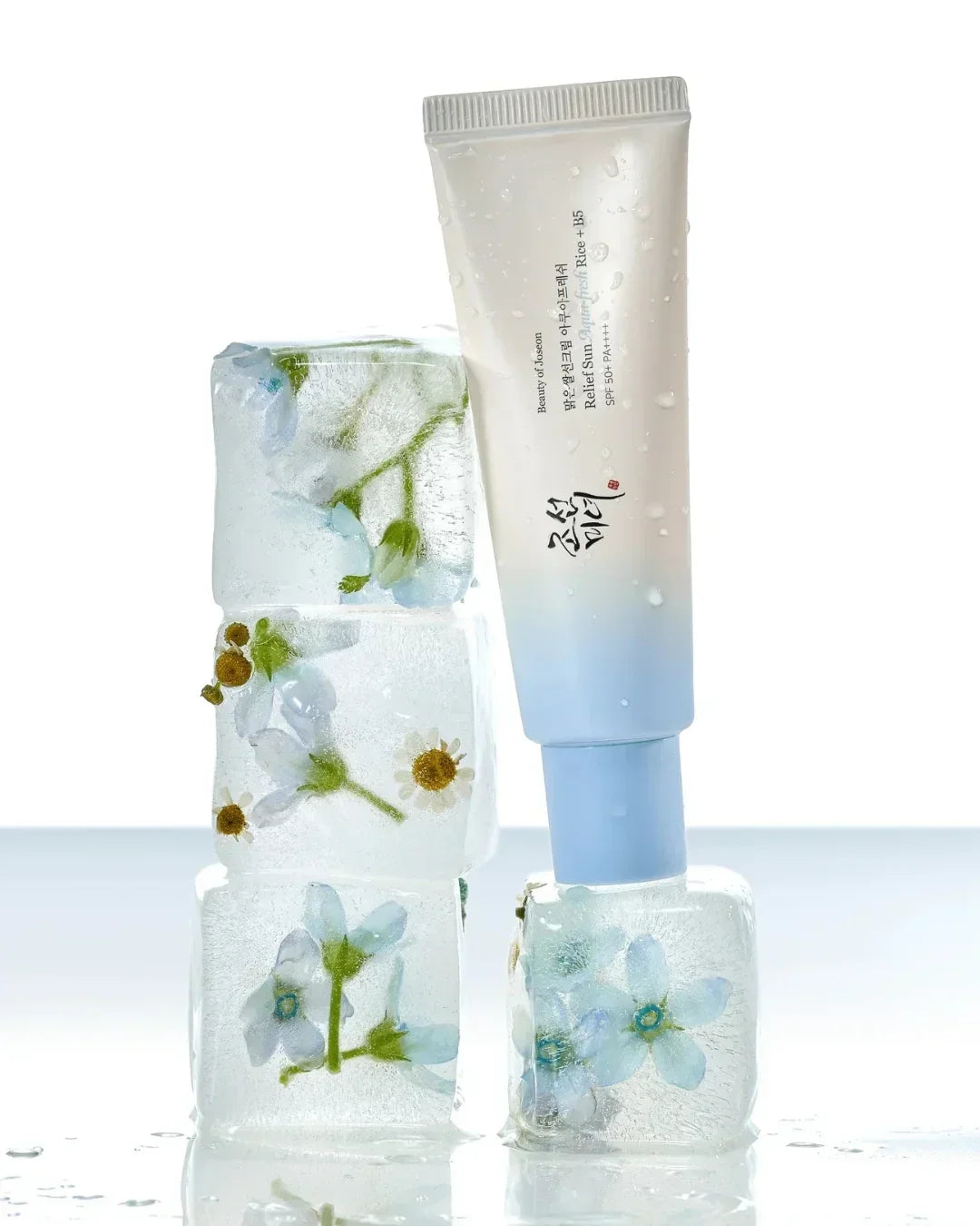 Relief Sun Aqua Fresh Rice B5 sunscreen tube with water droplets, surrounded by ice cubes with embedded blue and white flowers