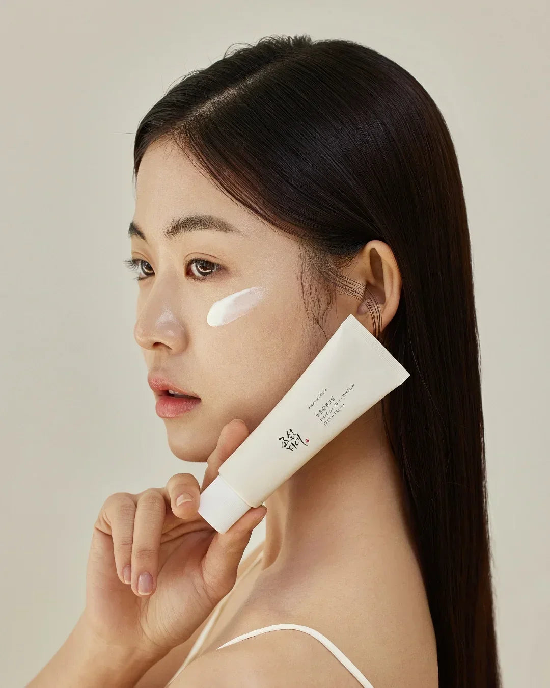 Asian woman with clear skin holding and applying Relief Sun Rice Probiotics SPF50+ PA++++ sunscreen cream