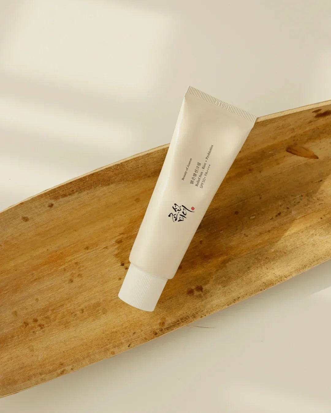 Relief Sun Rice Probiotics SPF50 PA++++ sunscreen tube on wooden tray with soft natural light